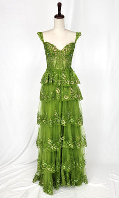 The Chicas C2433 Tiered Long Ruffle Prom Dress is a floor-length, sleeveless green gown with floral embroidery and layered ruffles, displayed on a dress form against a white background.