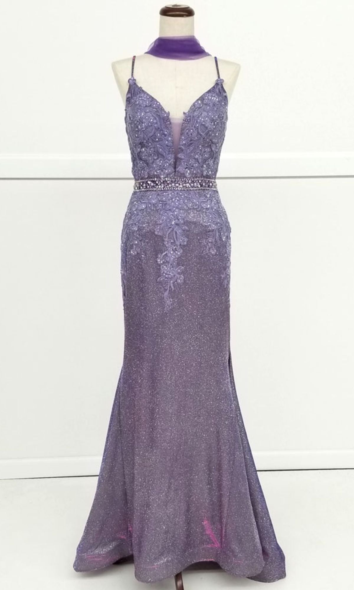 Displayed on a dress form is the Chicas C243 Low-Back Long Mermaid Prom Dress—a formal, sleeveless floor-length purple gown with a deep V neckline, beaded belt, lace detailing, and matching choker for an elegant look.