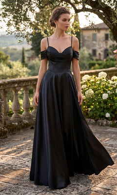 A woman wearing the Long Prom Dress: Chicas C2575 in black, featuring an elegant off-the-shoulder neckline, stands outdoors on a stone terrace surrounded by greenery and flowers.
