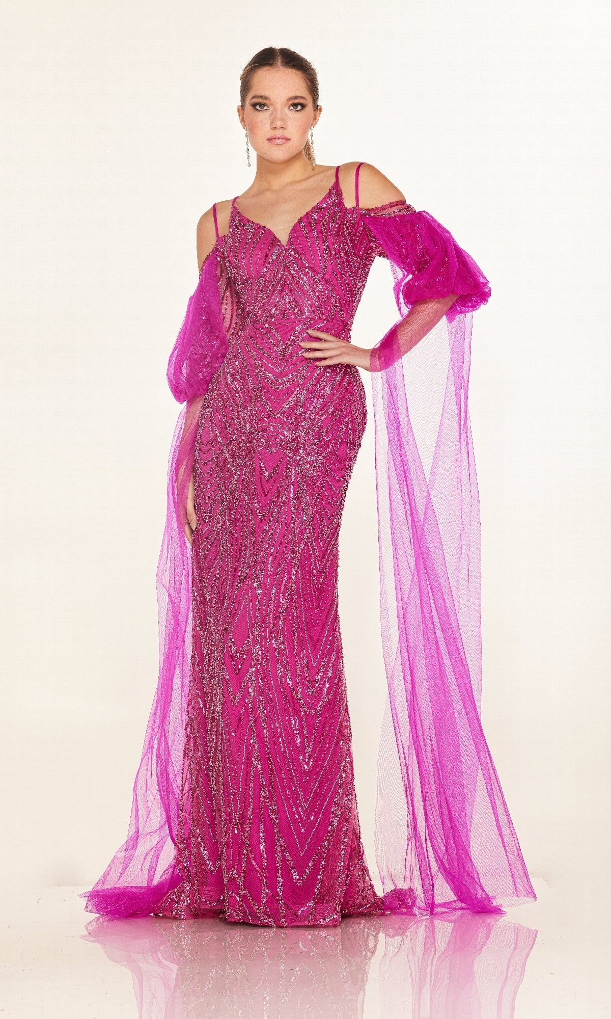 A woman wears the Cecilia Couture C270, a fitted long formal dress in bright magenta with sparkly embellishments, sheer off-the-shoulder sleeves, and flowing tulle drapes.
