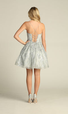 A woman faces away wearing the Lace-Up Glitter-Print Short Homecoming Dress C317, a light gray A-line party dress with silver embellishments, lace-up back, and spaghetti straps. She pairs it with silver heels.