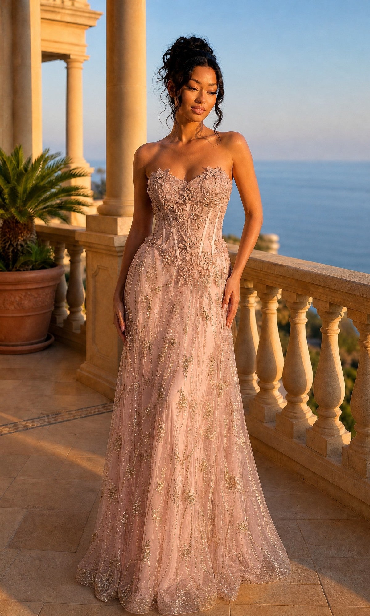 A woman in the Chicas C329 long prom dress with a strapless sweetheart neckline, corset bodice, and floral lace applique stands on a stone terrace with columns, overlooking the sea at sunset.