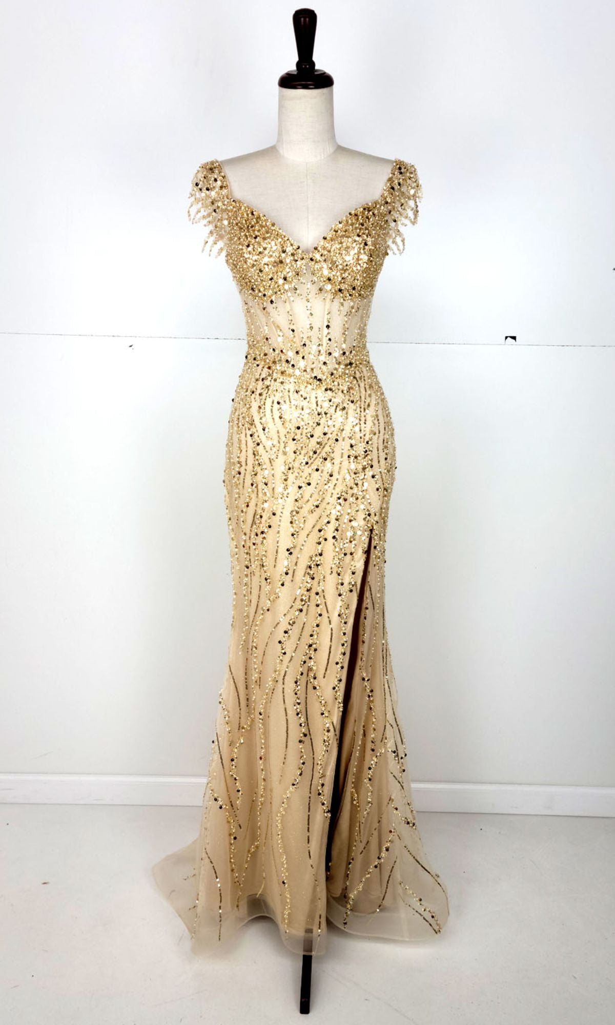 The Off-Shoulder Long Sequin Prom Dress: Chicas C331 features a floor-length, fitted champagne design with gold bead embellishments, off-the-shoulder sleeves, and a front slit, shown on a dress form against a plain background.