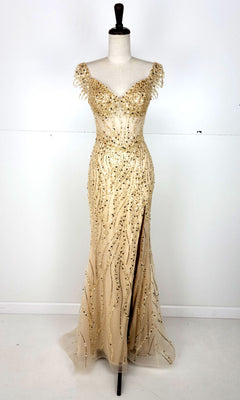 The Off-Shoulder Long Sequin Prom Dress: Chicas C331 features a floor-length, fitted champagne design with gold bead embellishments, off-the-shoulder sleeves, and a front slit, shown on a dress form against a plain background.