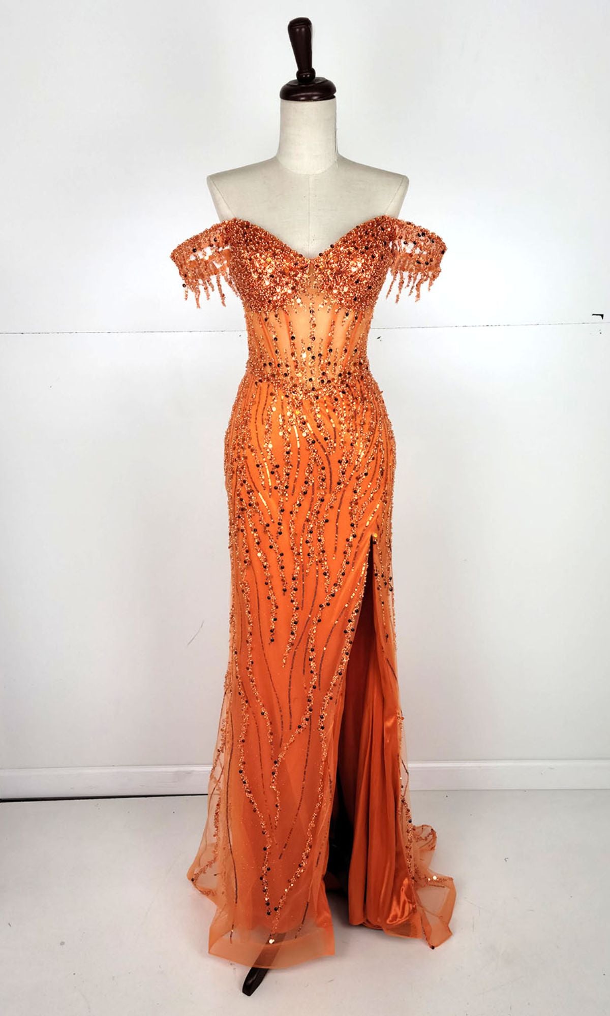 The Off-Shoulder Long Sequin Prom Dress: Chicas C331 is an orange gown with bead embellishments, a sweetheart neckline, sheer sleeves, and a thigh-high slit, displayed on a dress form against a white background.