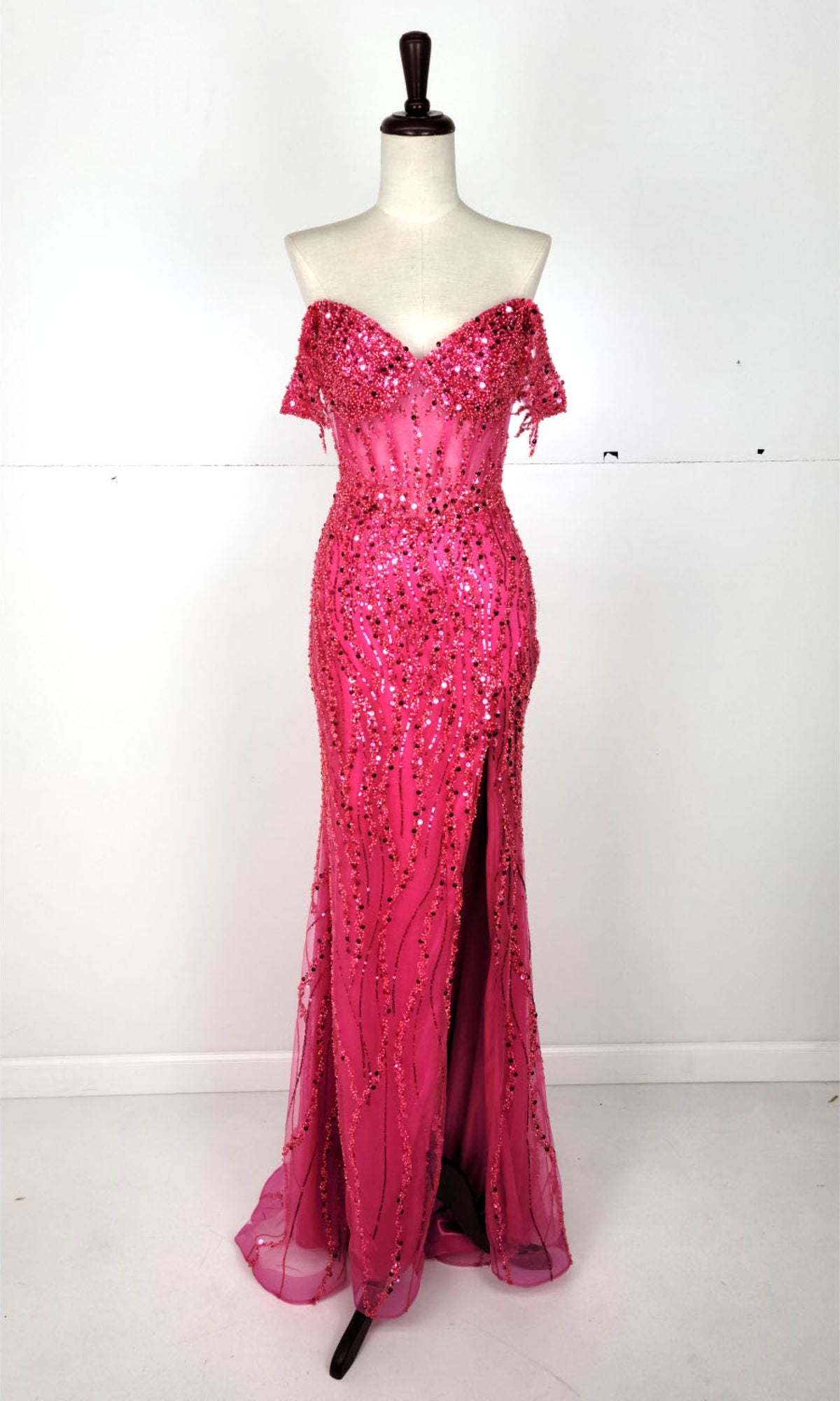 A mannequin showcases the Chicas C331 Off-Shoulder Long Sequin Prom Dress in hot pink with a front slit, set against a plain white background—an eye-catching evening gown ideal for formal events.