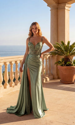 A woman wearing the Long Prom Dress: Chicas C342 in light green satin with sheer details and a thigh-high slit stands on a terrace with columns, overlooking the ocean and a potted palm.
