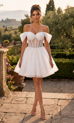 Wearing the Chicas C363 Short Homecoming Dress in Off White, a woman stands outdoors on a stone path in a garden. The elegant A-line design features a short, off-the-shoulder neckline with a sheer corset bodice and tulle skirt.