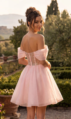 Wearing the Chicas C363 short homecoming dress, a woman stands outdoors amidst greenery and mountains, smiling as she looks back. The off-the-shoulder design and elegant A-line silhouette are complemented by the light pink, short tulle skirt.