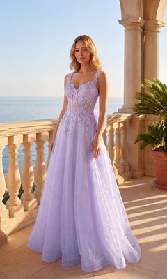 A woman in a lilac Chicas C379 long prom dress with a corset bodice stands on a sunlit balcony overlooking the sea, surrounded by stone columns and a potted palm.