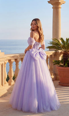 A woman in the Chicas C386 long prom dress, featuring a lavender off-the-shoulder design with a large bow, stands on a terrace overlooking the ocean.