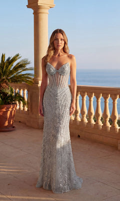 A woman stands on a balcony by the sea, wearing the Long Prom Dress: Chicas C387 in silver, featuring a strapless, fitted semi-sheer corset bodice and a flowing long skirt adorned with sequins.