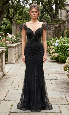 A woman stands on a stone pathway in a garden, wearing the Long Formal Dress: Chicas C390, which features sheer cap sleeves and geometric bead detailing.