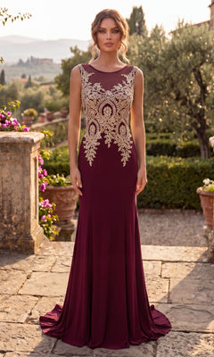 A woman wearing the Gold-Embroidered Long Prom Dress, Chicas C4233 in burgundy, with a sleeveless design and gold embroidered bodice, stands on a stone walkway in a garden setting during daylight.