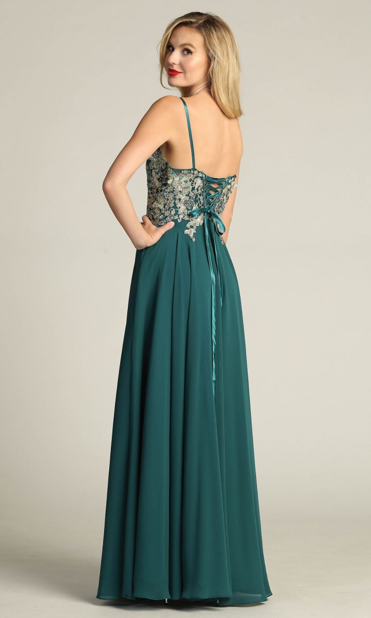 A woman wears the Chicas C5124 Lace-Up Open-Back Long Prom Dress, featuring a teal A-line silhouette, thin straps, floral embroidered bodice, lace-up back, and pockets, as she looks over her shoulder.