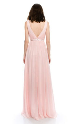 A woman stands with her back to the camera in a sleeveless, floor-length light pink Chicas C7818 prom dress, featuring a deep V-back and an A-line silhouette against a white background.