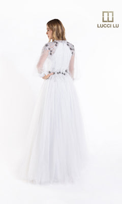 A woman faces away wearing the Lucci Lu C8057, a white long-sleeve formal A-line dress with lace, beads, a sheer sleeve, and fitted bodice. The Lucci Lu logo is in the top right corner.