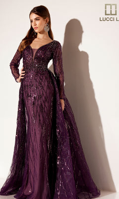 A woman stands elegantly against a light background wearing the Lucci Lu C8095, a long formal dress in deep purple with sequin detailing and a sheer tulle overskirt.