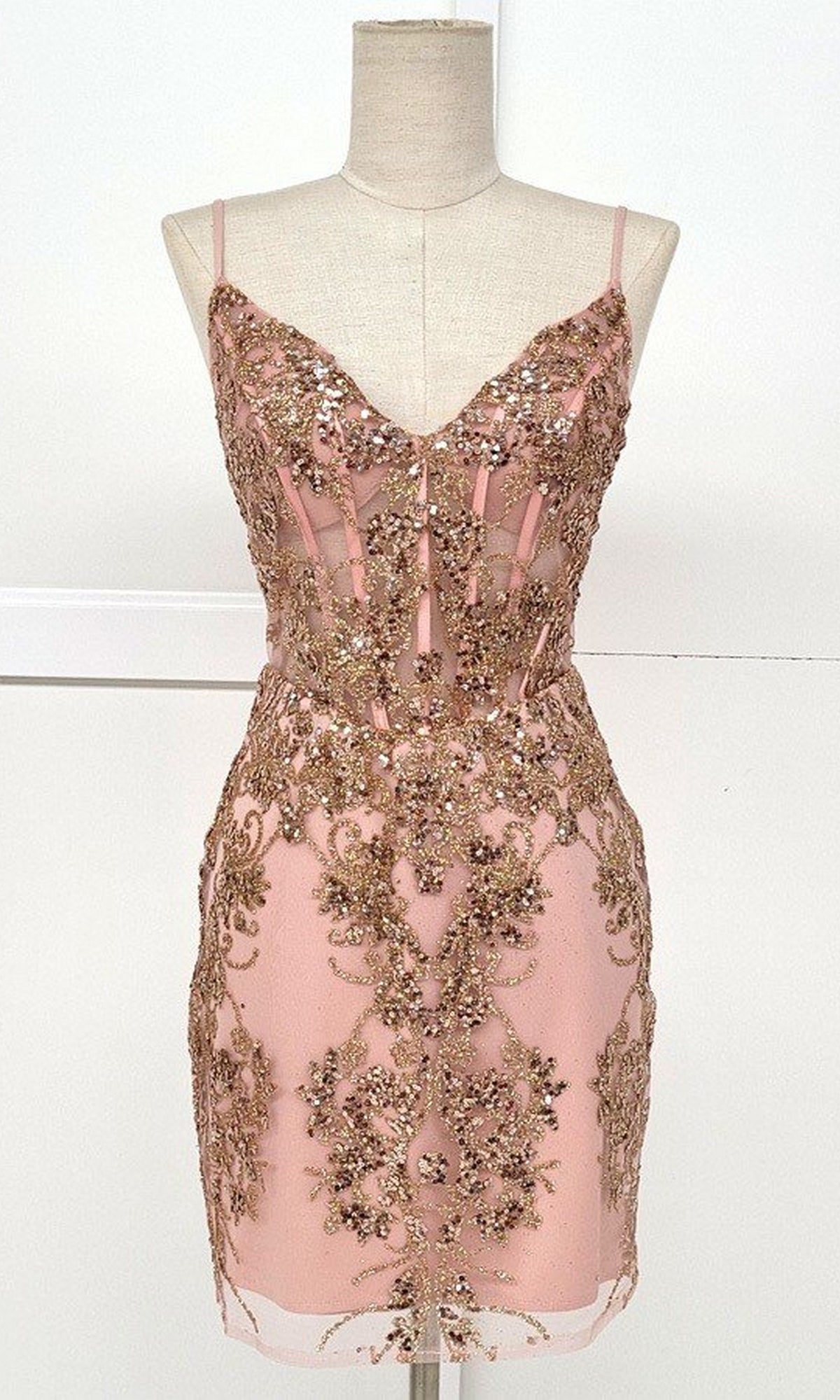 The Sheer-Corset Short Glitter Homecoming Dress C814 is a blush pink sleeveless semi-formal dress with thin straps, gold sequin and bead embellishments, and a fitted silhouette displayed on a dress form.