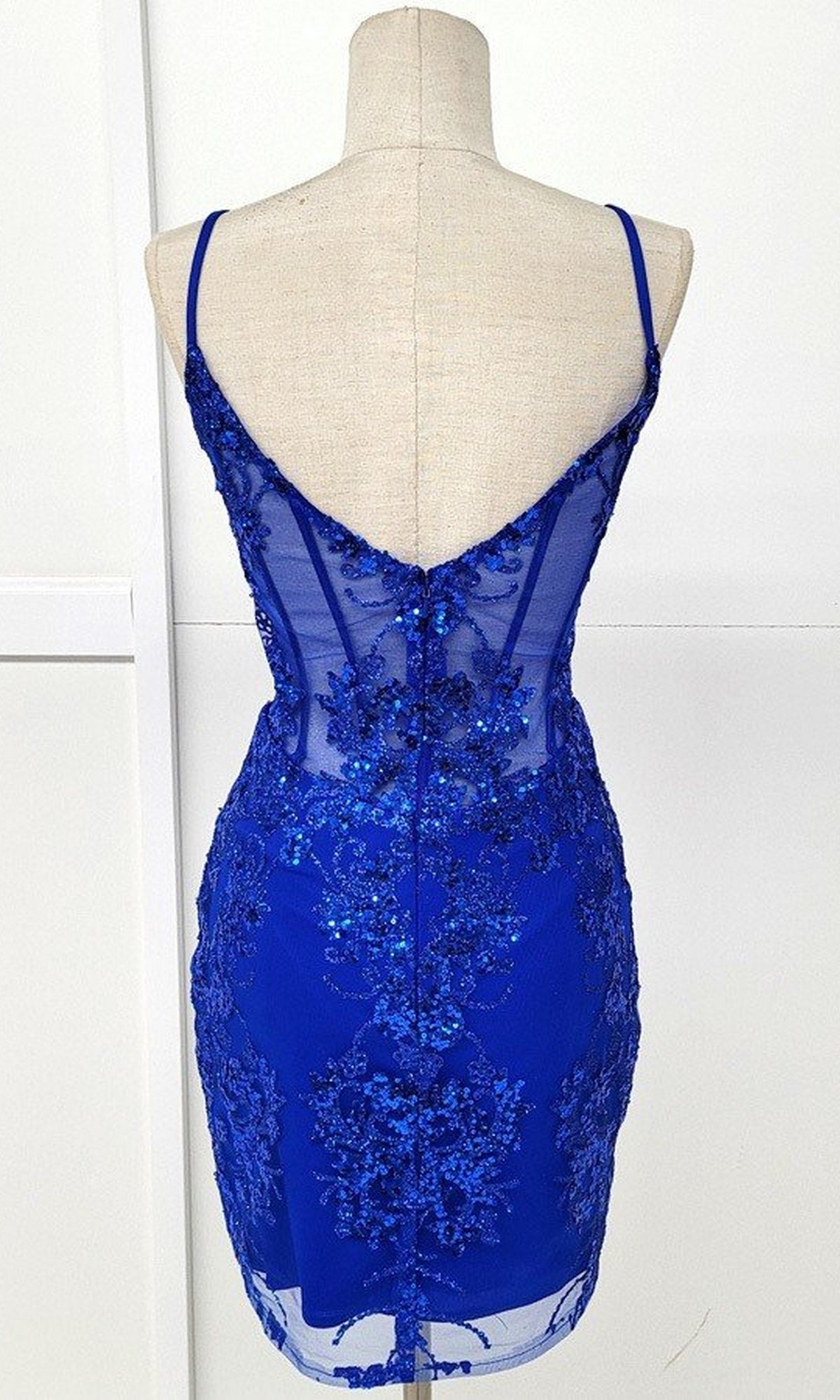 A mannequin displays the Sheer-Corset Short Glitter Homecoming Dress C814 in royal blue, featuring a sleeveless design, sheer back, sequin and lace embellishments, and thin spaghetti straps.