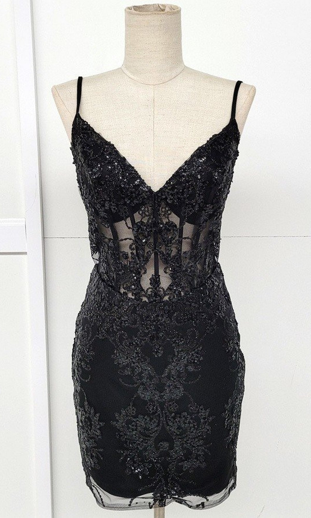 The Sheer-Corset Short Glitter Homecoming Dress C814 is a black sleeveless mini dress with thin straps, a V-neckline, and sparkling lace and sequin details—an eye-catching semi-formal look shown on a mannequin.
