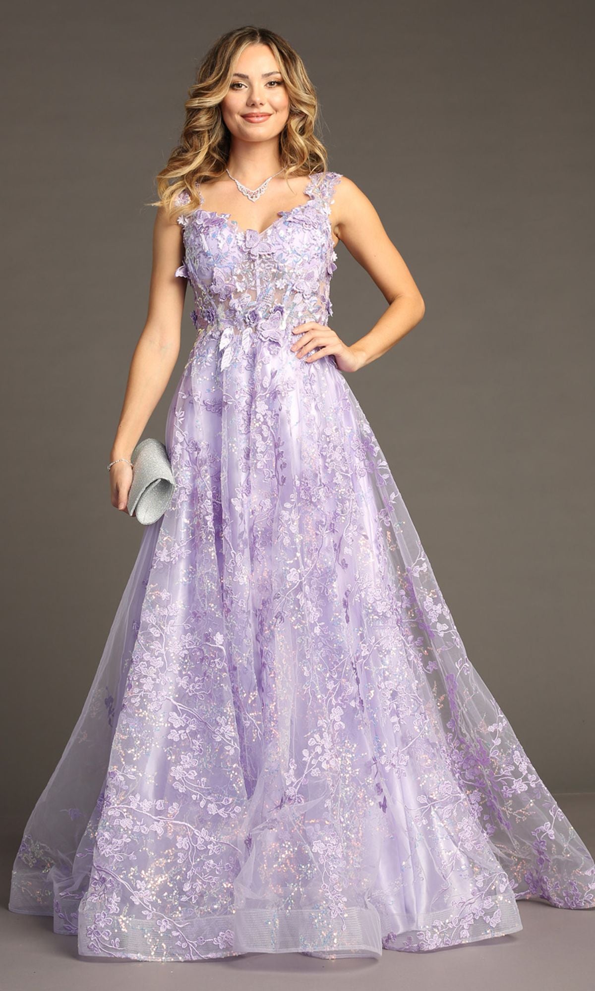 A woman poses against a plain background in the Floral-Print Lace-Up Long Prom Dress: Chicas C818, a sleeveless lavender gown with a corset-style bodice and floral embroidery, smiling and holding a silver clutch.