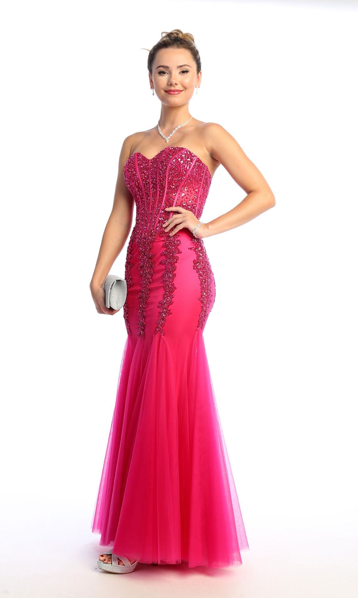 A woman wearing the Strapless Long Mermaid Prom Dress: Chicas C820 in bright pink with sequin details holds a silver clutch and poses against a white background.