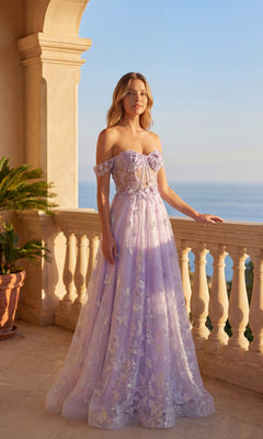 On a sunlit balcony overlooking the sea, a woman wears the Long Prom Dress: Chicas C822 in lilac, adorned with delicate floral embellishments and featuring an off-the-shoulder design.