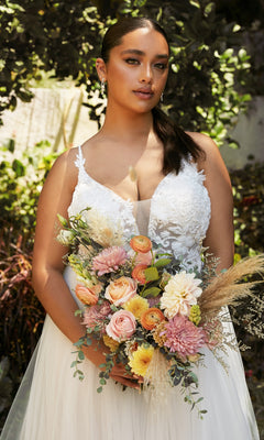A woman in a Classic Off-White Long Prom Dress: Ladivine CB072W holds a bouquet of pastel flowers and greenery, standing outdoors with lush foliage in the background.
