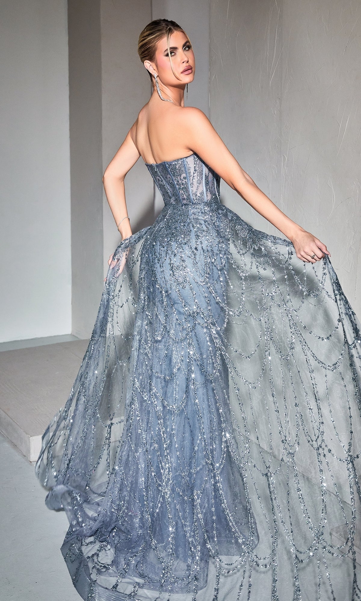 A woman poses in the Strapless Mermaid Prom Dress with Overskirt CB095—a floor-length, blue-gray gown featuring a sheer, glittering overlay and intricate beaded patterns.