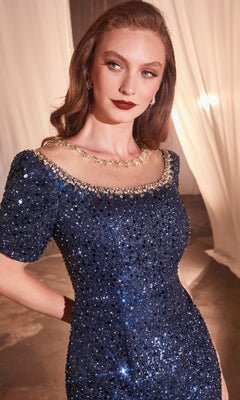 A woman wears the Ladivine CB151 short-sleeve sequin formal dress in navy blue, accessorized with a gold necklace and earrings, standing indoors with draped white fabric in the background.