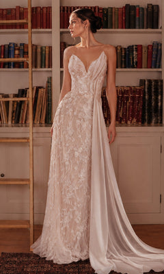 A woman in an off white/nude Long Prom Dress by Ladivine (CB168W), featuring a sleeveless design with delicate floral lace appliques and a draped train, stands in front of bookshelves filled with books.