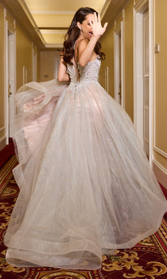 A woman in the Ladivine CC2531 long silver A-line prom dress stands in a hallway, looking back and raising one hand to partially cover her face.