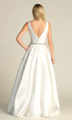 A woman stands with her back to the camera, wearing the Jeweled-Waist Long Prom Ball Gown Chicas CC3021—a sleeveless white A-line dress with an embellished waistband and a deep V-back.