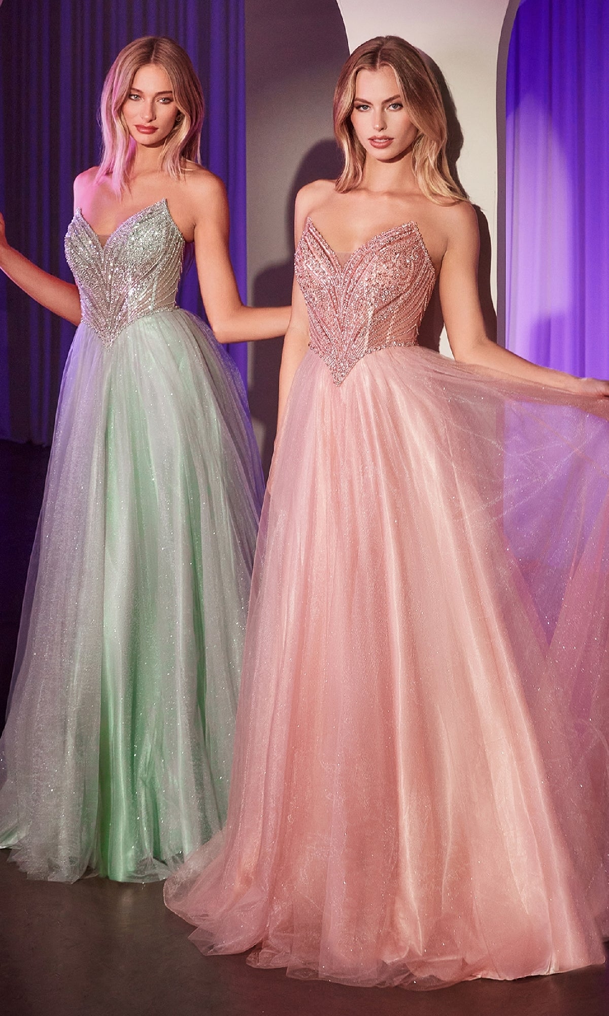 Two women stand side by side in a softly lit room, radiating elegance in the Ladivine CC415 Beaded-Bodice Long Prom Dress—one in light green and one in light pink—each showcasing the gown’s sparkling strapless a-line design.