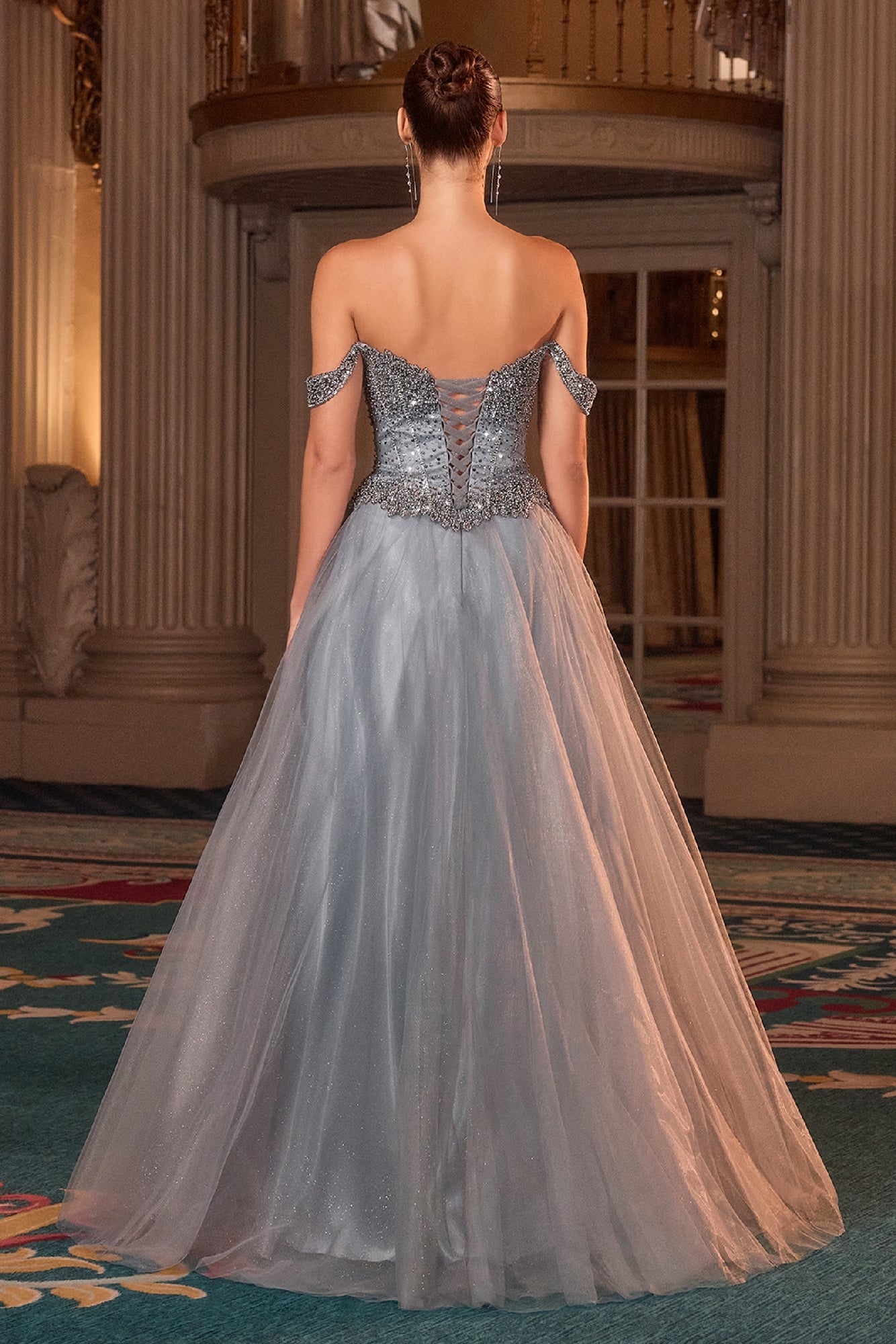 Woman in a glitter tulle evening gown with intricate detailing in an elegant indoor setting.
