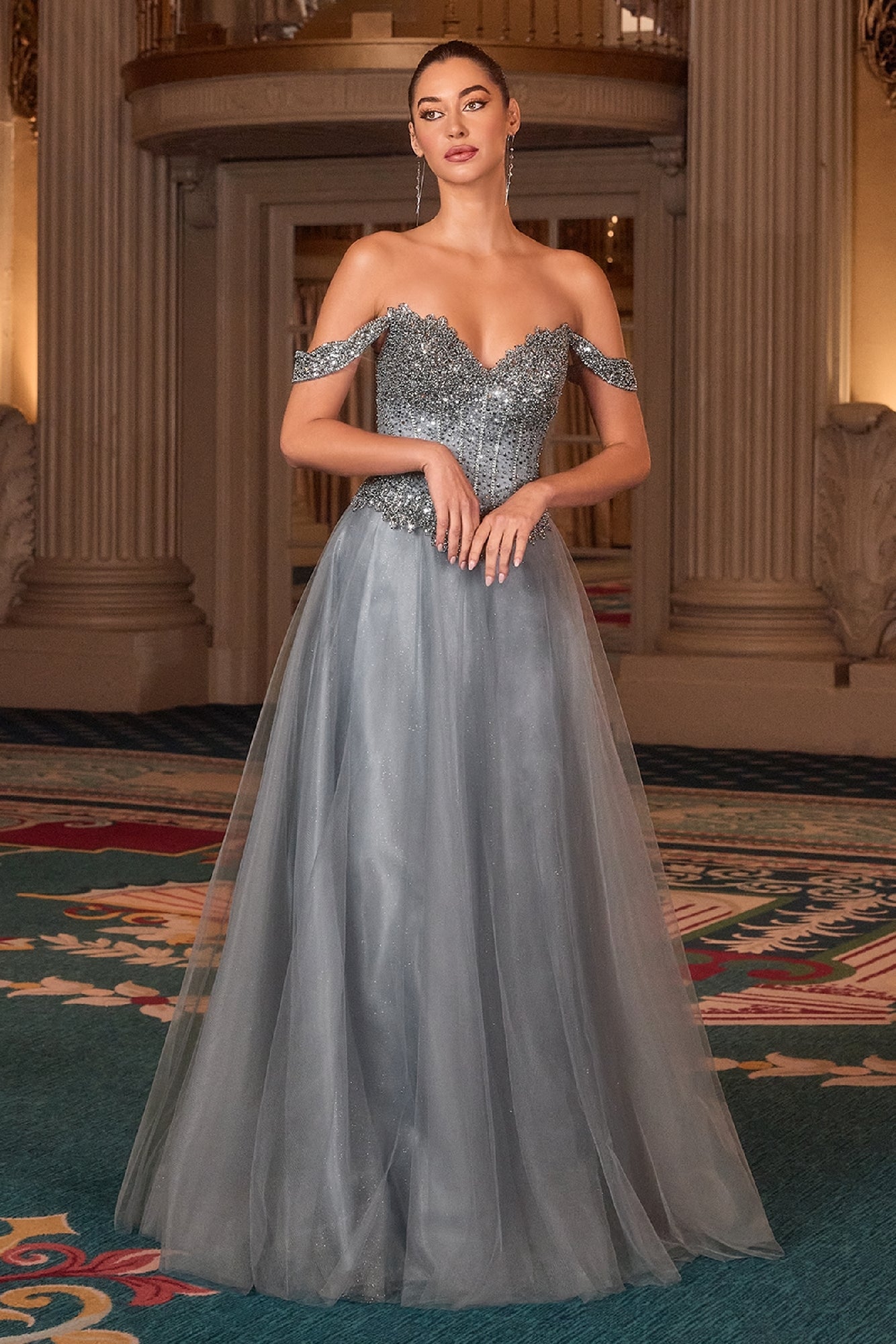Woman in a glitter tulle evening gown standing in an elegant room with decorative columns and carpet.
