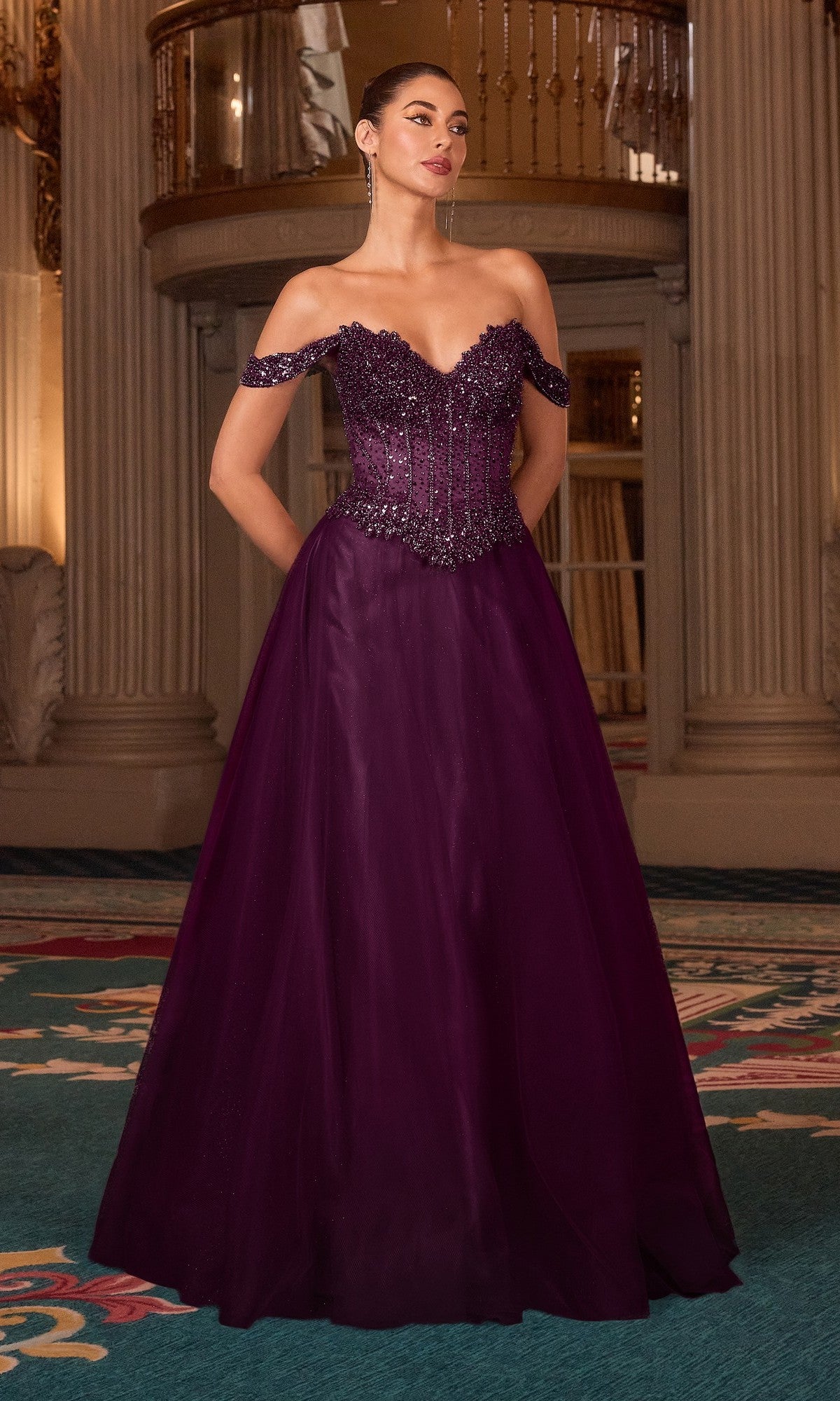 A woman stands indoors wearing the Off-the-Shoulder Glitter Prom Gown: Ladivine CC471 in deep purple, featuring a beaded bodice and full skirt.