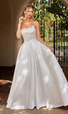 A woman in the Ladivine CC511W long formal dress in off white, featuring a strapless embroidered corset bodice and flowing A-line silhouette, stands outdoors before ornate wrought iron gates.