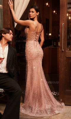 A woman in the Long Pearl Corset Prom Dress: Ladivine CC8801 stands by a suited man in a dimly lit, elegant venue, her blush pink lace-up gown embellished with beads and pearls sparkling in the light.