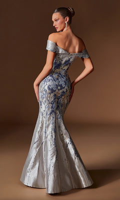 A woman models the Ladivine CD0107 long formal dress, featuring an off-the-shoulder silver and blue jacquard mermaid silhouette, as she poses against a plain brown background.