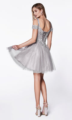 A woman poses in the Cold-Shoulder Short Glitter Homecoming Dress CD0132, a silver off-shoulder party dress with a lace-up back and tulle skirt, holding the skirt and finishing her look with high-heeled sandals.