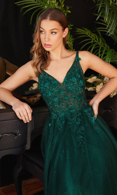 A woman in the Glitter Tulle Illusion Prom Dress: Ladivine CD0181, dark green and embroidered, sits by a black piano adorned with flowers, surrounded by lush green plants.