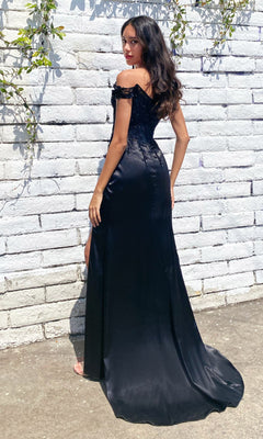 A woman stands outdoors on concrete in front of a white brick wall with green vines, wearing the Off-the-Shoulder Long Sweetheart Prom Dress CD0186, which features stunning glittery embroidery.