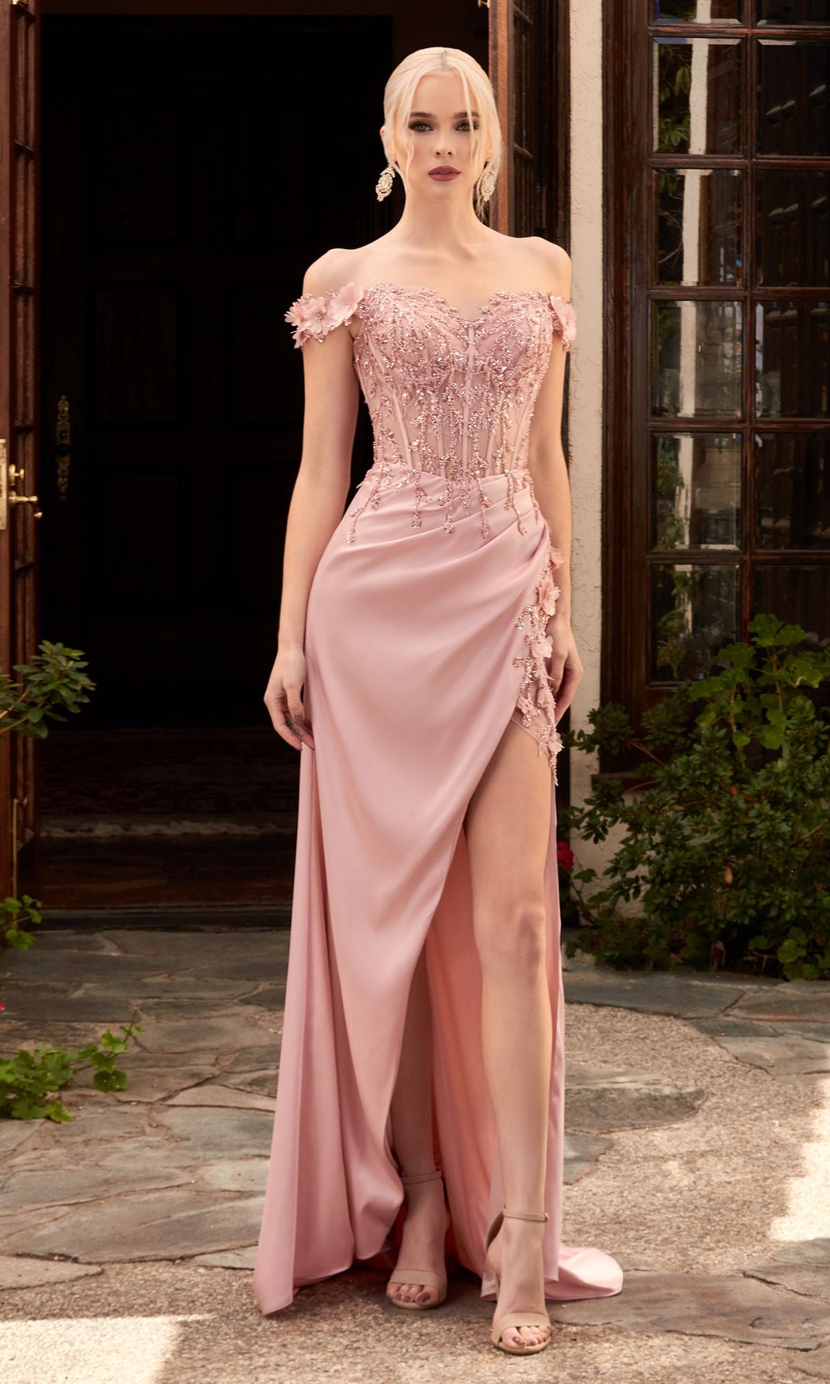 A woman stands outdoors wearing the Off-the-Shoulder Long Sweetheart Prom Dress CD0186—a light pink gown with a beaded bodice, glittery embroidery, floral appliqué, and thigh-high slit—paired with matching high-heeled sandals.