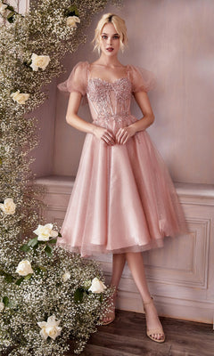Wearing the blush pink, sparkly Puff-Sleeve Tea-Length Prom Dress: CD0187, a woman stands beside a floral arrangement of white roses and baby's breath against a pale wall.