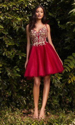 A woman stands outdoors before green foliage, wearing the affordable Glitter-Tulle Short A-Line Prom Dress CD0188 in red with thin straps, floral embroidery, and nude heels.