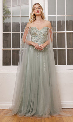 A woman stands indoors on a wooden floor in front of large windows, wearing the Cape-Sleeve Long Beaded Prom Dress CD0204 with silver sequins and sheer tulle cape sleeves.