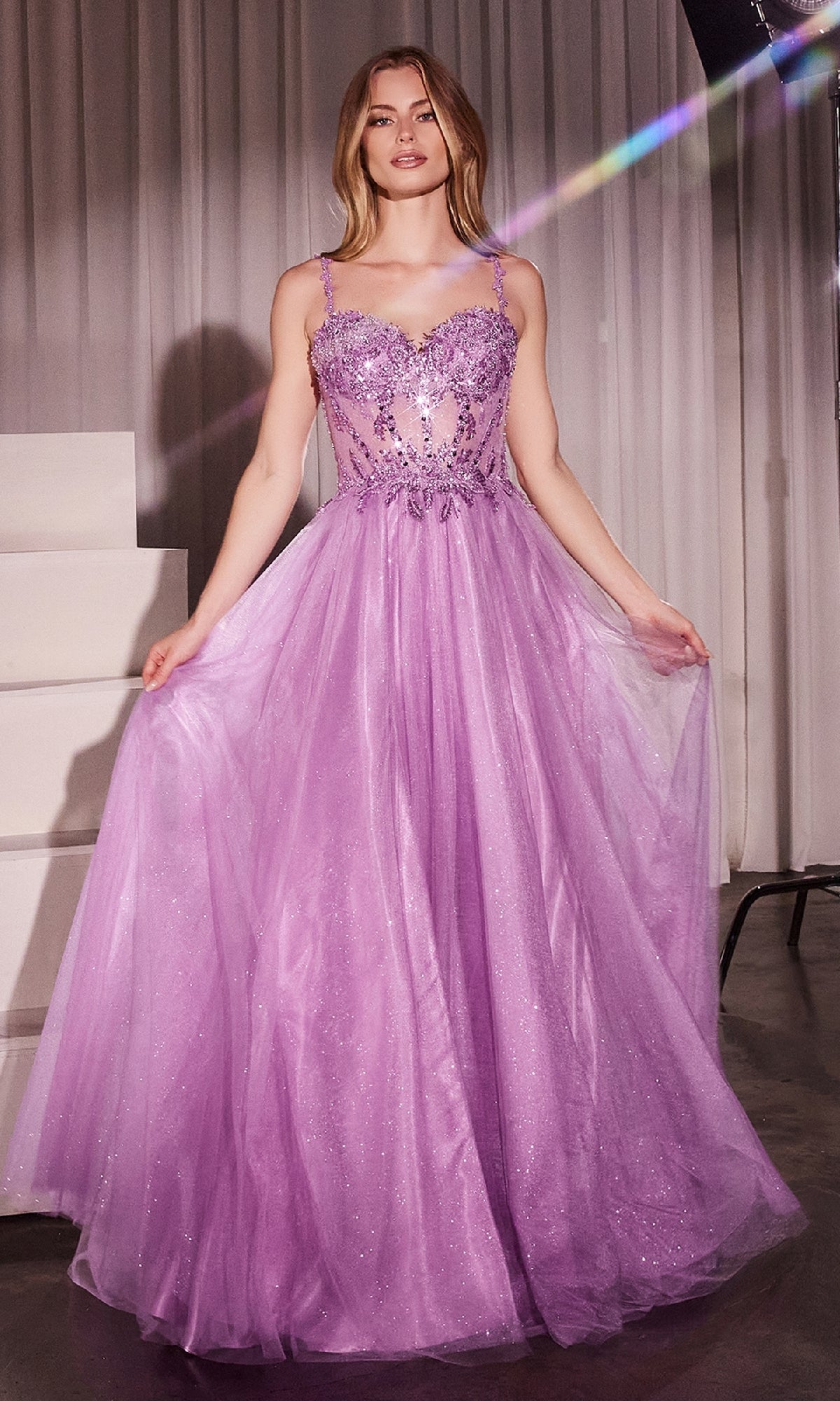 A woman stands indoors wearing the Glitter-Tulle Long Prom Dress: Ladivine CD0234, featuring a lace-up back, embellished sweetheart bodice, and a flowing glitter-tulle overlay with sparkling details.