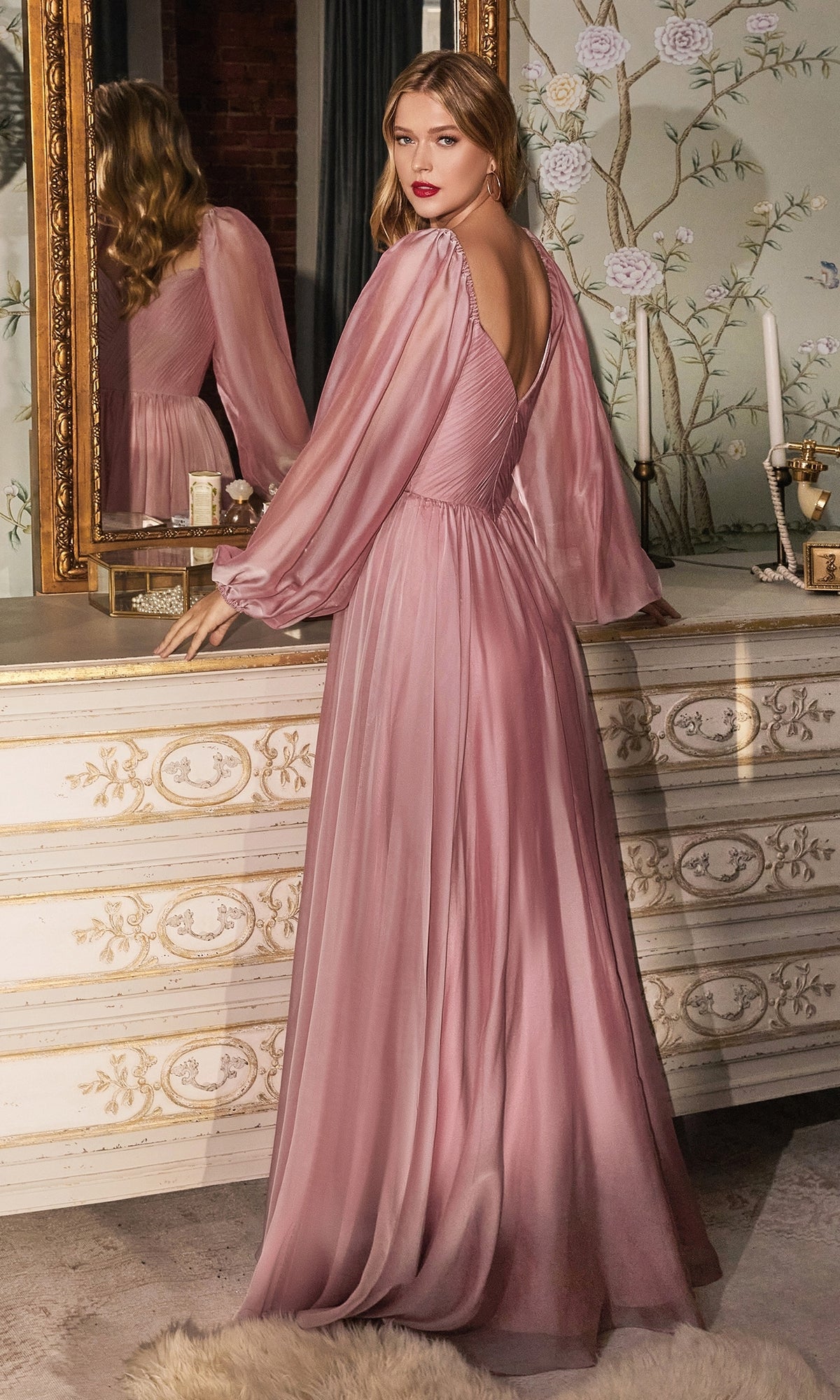 Wearing the Ladivine Long Bishop-Sleeve Prom Dress CD243 in sheer mauve, a person stands by an ornate dresser, gazing over their shoulder toward a mirror.